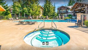 A pool area with a hot tub, lounge chairs, and a building with a stone facade.