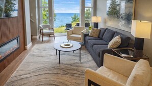 A modern living room with a large window overlooking the sea, a fireplace, and a cozy seating area with a sofa and armchairs.