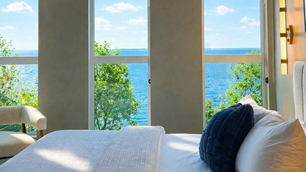 A bedroom with a large bed, a view of the sea, and a chair.