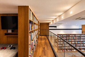 A modern library with wooden bookshelves, a flat-screen TV, and a staircase leading to another level. - Nidra Niwas (Jaipur)