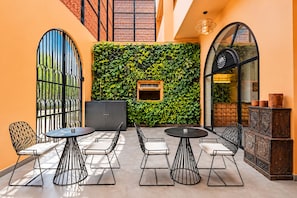 A modern outdoor seating area with round tables and metal chairs, a green vertical garden wall, and a wooden cabinet with decorative items. - Nidra Niwas (Jaipur)