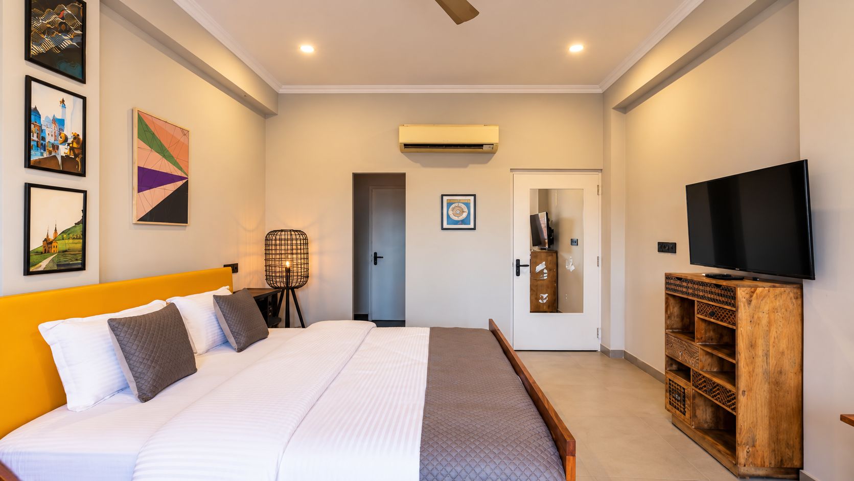 Une chambre d’hôtel avec un lit, une télévision, une armoire en bois et des œuvres d’art accrochées aux murs.