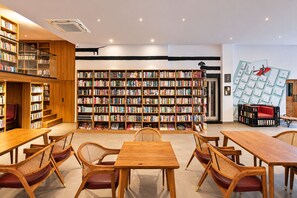 Una biblioteca con múltiples estanterías de madera, un área central con mesas y sillas, y una instalación artística original en la pared.