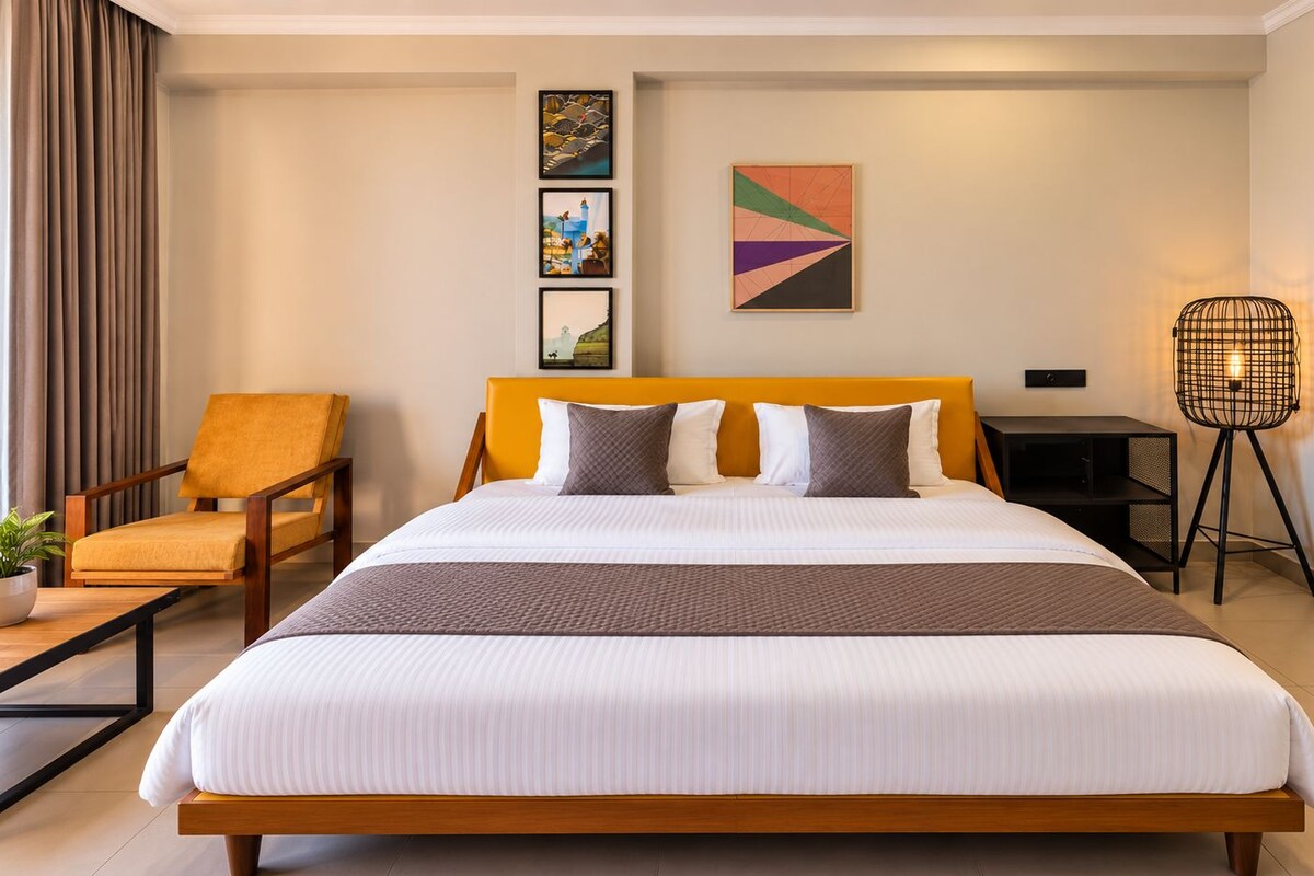A hotel room with a large bed, a chair, a bedside table, a lamp, and artwork on the wall.