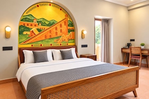 A hotel room with a bed, a desk with a chair, and a large mural on the wall. - Nidra Niwas (Jaipur)