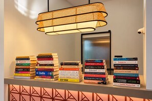 Una estantería con varios libros, una lámpara colgante de ratán y una pared con un diseño geométrico.