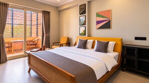 Een hotelkamer met een groot bed, een eettafel, stoelen, een balkon met uitzicht en kunstwerken aan de muren.