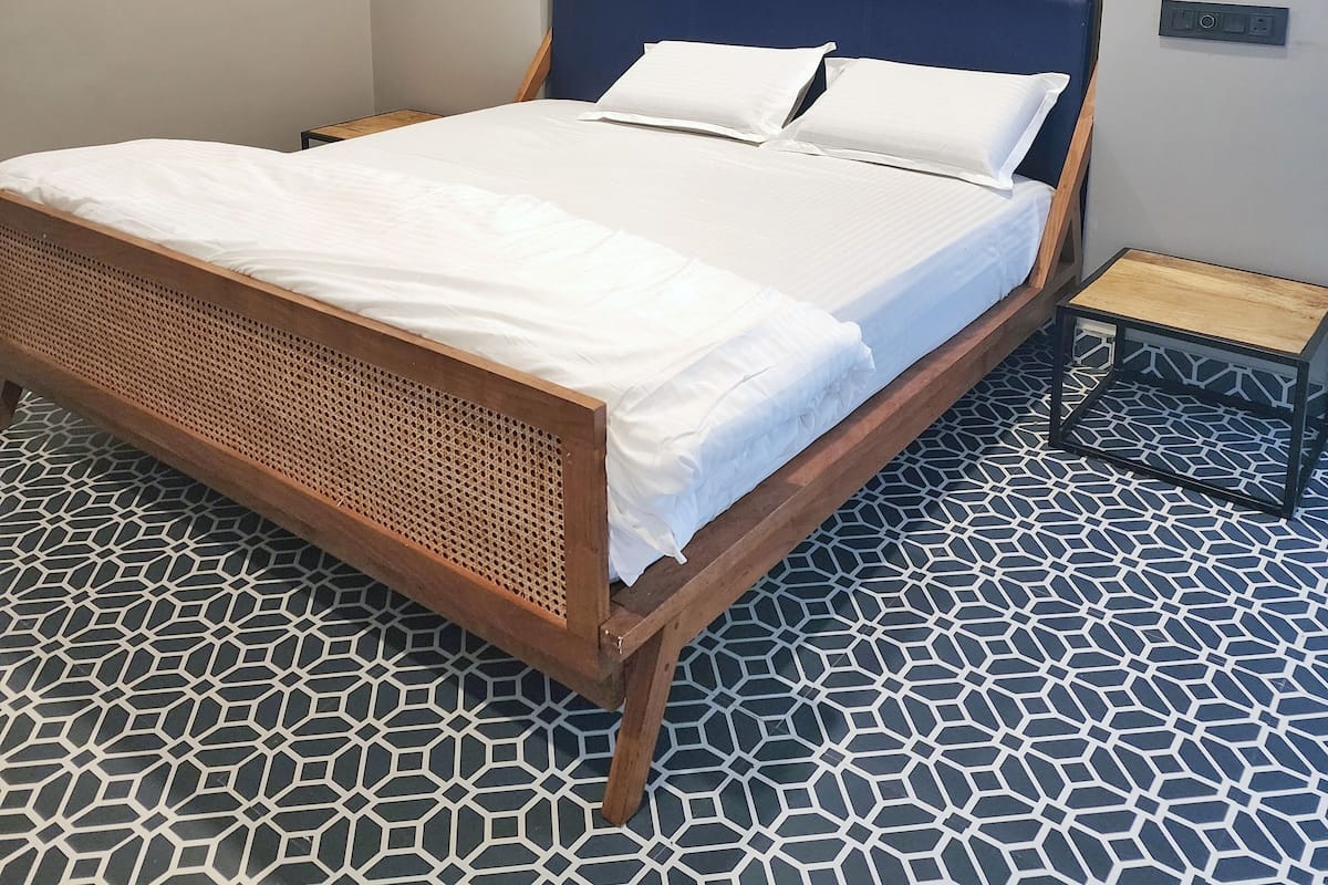 A bed with a wooden frame and a white mattress, a wall-mounted air conditioner, a decorative mural, and a patterned floor.