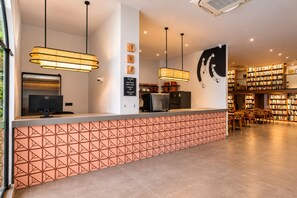A reception desk with a geometric patterned counter, a computer, and a coffee machine. There are wall-mounted clocks and a welcome sign. - Nidra Niwas (Jaipur)