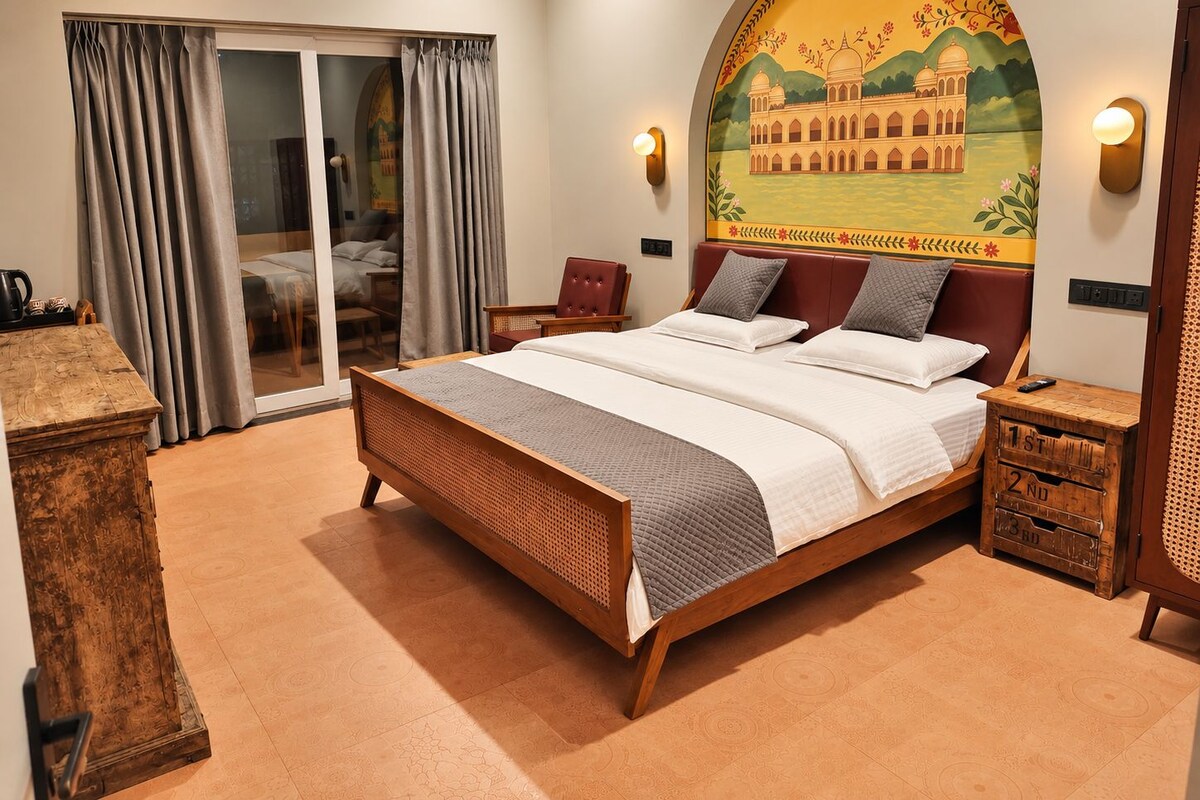 A hotel room with a large bed, a sliding glass door to a balcony, and a mural of a building on the wall.