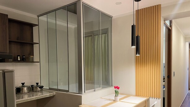 A modern kitchen with a glass partition, a wooden dining table with chairs, and a small potted plant.