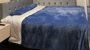 A bedroom with a tufted headboard, a bed with a blue and white bedspread, a bedside table, and a mirror on the wall.