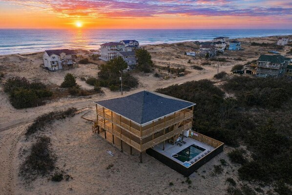Une propriété située en bord de mer, comprenant un grand bâtiment, une piscine et offrant une vue sur l’océan et la plage.