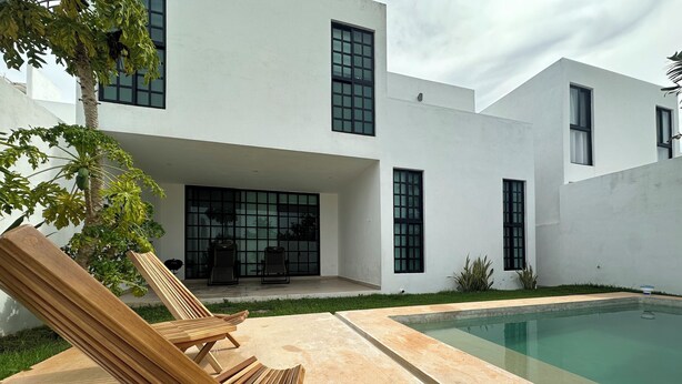 Una casa moderna con piscina, due poltrone relax e un patio.