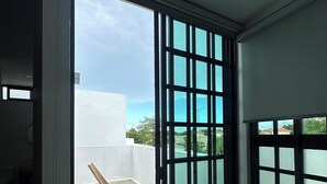 Una stanza con un'ampia porta-finestra scorrevole che dà su un balcone con vista sul cielo e edifici in lontananza.