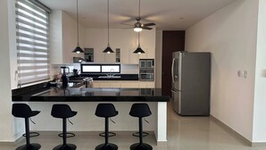 Una cucina moderna con isola centrale, sgabelli da bar, frigorifero e ventilatore a soffitto.