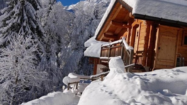 A wooden cabin with a snow-covered roof, surrounded by snow-laden trees and mountains. - Le Refuge Des Marmottes (BEAUFORT)