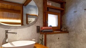 A bathroom with a wooden vanity, a large oval sink, a mirror, a toilet, and a small window. - Le Refuge Des Marmottes (BEAUFORT)