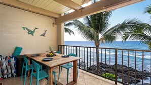 Un patio techado con una mesa y sillas de madera, vista al océano y una barandilla.
