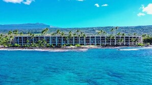 Un hotel frente a la playa con varias edificaciones, palmeras y una vista despejada del océano.
