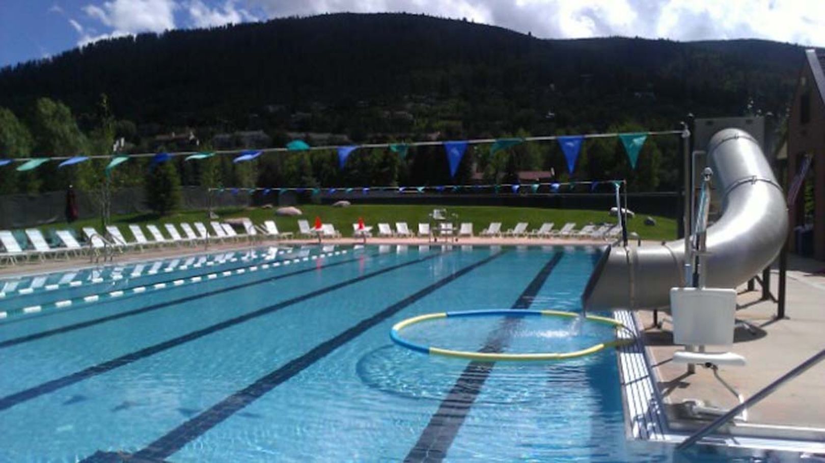 Ein Schwimmbecken mit Bahnen, einer Wasserrutsche und Liegestühlen.