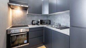 Eine moderne Küche mit dunklen Schränken, einem eingebauten Backofen, einem Kochfeld, einer Spüle und einer Kaffeemaschine.