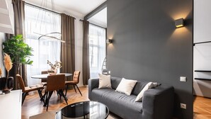 Ein modernes Wohnzimmer mit grauem Sofa, einem runden Glastisch und einem Essbereich mit rundem Tisch und Stühlen.