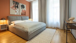 Une chambre à coucher moderne avec un grand lit, deux tables de chevet avec des lampes, un tapis à motifs et un tableau au mur.