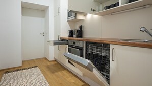 Une cuisine de taille réduite, dotée de meubles blancs, d’un four à micro-ondes, d’une machine à café et d’un lave-vaisselle.