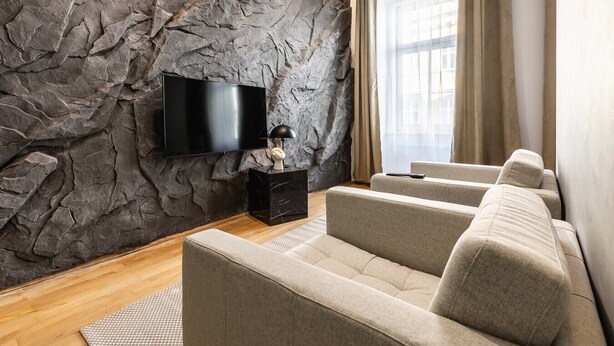 A modern living room with a stone wall, a flat-screen TV, a black side table, and a beige sofa. - Posh and stylish apartment with a queen-size bed (Wien)