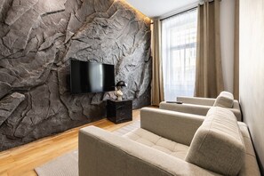 Un salon moderne avec un mur en pierre, un téléviseur à écran plat, une table d’appoint noire et un canapé beige.