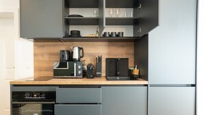 Eine kompakte Küche mit einer Holzausziehtafel, einer Kaffeemaschine, einem Toaster und einem Wasserkocher.