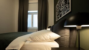 Ein Hotelzimmer mit Bett, Nachttisch, Lampe und einem Fenster mit Vorhängen.