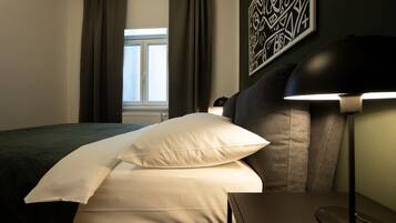 Ein Hotelzimmer mit Bett, Nachttisch, Lampe und einem Fenster mit Vorhängen.