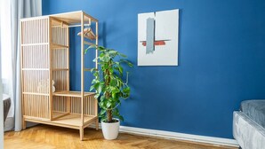 Una habitación con pared azul, una estantería de madera, una planta en maceta y una cama.