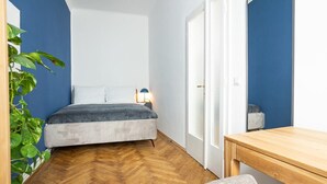 Un dormitorio con una cama, una mesita de noche con lámpara, un escritorio de madera y una silla.