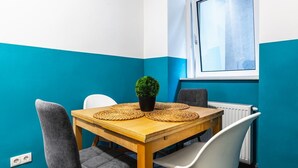 A room with teal walls, a wooden table with woven placemats, a potted plant, and a window with a view. - Precious apartment in calm district area (Wien)