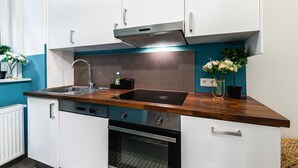 A modern kitchen with white cabinets, a stainless steel sink, a black induction cooktop, and a built-in oven. - Precious apartment in calm district area (Wien)