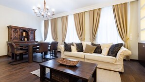 Een woonkamer met een bank, salontafel, eettafel, stoelen en een kroonluchter.