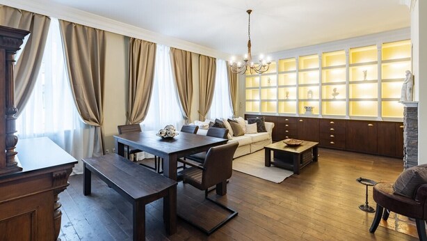Een moderne woonkamer met een eethoek, houten meubels, een kroonluchter en een open haard met een glazen vitrine.