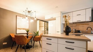 A modern kitchen with white cabinets, a wooden countertop, and a dining area with chairs and a table. - Cosy, brand new 2-bedroom apartment (Wien)