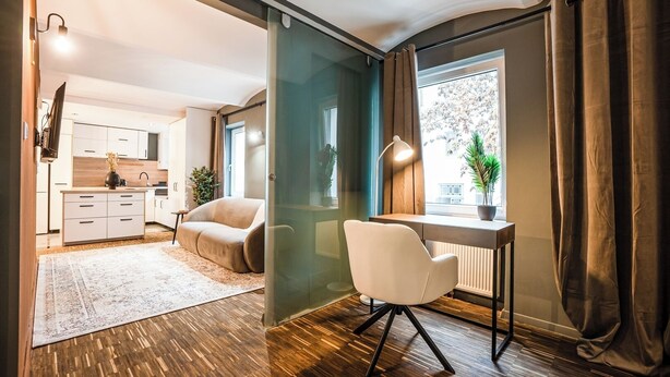A modern living space with a kitchen, a sofa, a desk, and a large window with curtains. - Cosy, brand new 2-bedroom apartment (Wien)