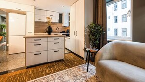 A modern kitchen with white cabinets, a Bosch refrigerator, and a dining area with a sofa and a small table. - Cosy, brand new 2-bedroom apartment (Wien)