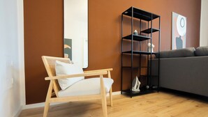 Ein modernes Wohnzimmer mit einem Holzstuhl, einem grauen Sofa, einem schwarzen Bücherregal und einem Spiegel an der Wand.