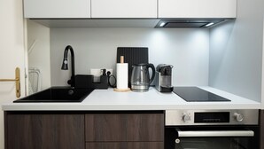 Eine moderne Küche mit einem schwarzen Spülbecken, einer Kaffeemaschine, einem Wasserkocher und einem Einbauofen.