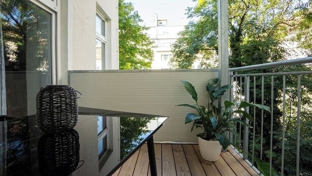 Un balcon avec une table en verre, des paniers en osier et une plante en pot.