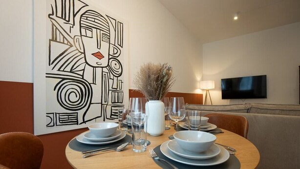 A dining area with a round table set for four, a modern abstract painting on the wall, and a flat-screen TV in the background. - Bright, modern and central flat with a terrace (Wien)