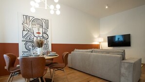 A modern living room with a dining area, a grey sofa, and a flat-screen TV mounted on the wall. - Bright, modern and central flat with a terrace (Wien)