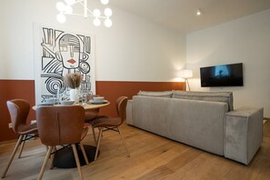A modern living room with a dining area, a grey sofa, and a flat-screen TV mounted on the wall. - Bright, modern and central flat with a terrace (Wien)