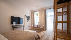 Een hotelkamer met een bed, een televisie, een bureau met stoel, een raam met gordijnen en een stapelbed.